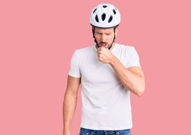 Bisiklet kaskı takan yakışıklı genç adam kendini iyi hissetmiyor ve soğuk algınlığı veya bronşitin belirtisi olarak öksürüyor. sağlık hizmeti kavramı. 