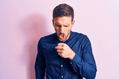 İzole edilmiş pembe arka plan üzerinde dikilen genç yakışıklı adam kendini kötü hissediyor ve soğuk algınlığı veya bronşitin belirtisi olarak öksürüyor. Sağlık hizmeti kavramı.