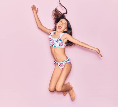 Tatildeki sevimli İspanyol kız bikini giyip ağzı açık gezerken şaşırdı. İzole edilmiş pembe arka plan üzerinden atlama