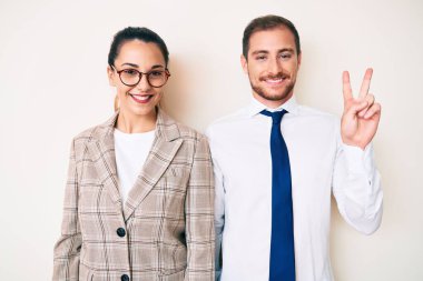 İş kıyafetleri giymiş güzel bir çift iki numarayı gösterip işaret ederken kendine güvenen ve mutlu bir şekilde gülümsüyor.. 