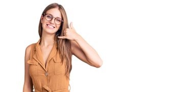 Genç, sarışın, sıradan kıyafetler ve gözlük takan, gülümseyen, el ve parmaklarıyla telefonla konuşan güzel bir kadın. iletişim kavramları. 