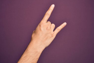 İzole edilmiş mor arka planda parmaklarını gösteren beyaz bir gencin eli. Rock 'n Roll sembolü, müstehcen boynuzlar gösteriyor.