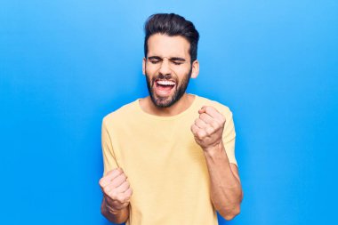 Sakallı, sıradan tişörtlü genç yakışıklı adam kolları havada ve gözleri kapalı bir şekilde başarıyı kutluyor ve şaşırıyor. 