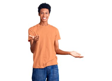 Genç Afrikalı Amerikalı günlük kıyafetler giymiş neşeli kollarını açıp gülümseyen bir adam. Hoş geldin, olumlu ve kendinden emin selamlar. 