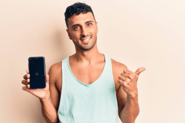Akıllı telefon tutan genç İspanyol adam ekranda mutlu ve pozitif gülümsüyor, başparmağıyla mükemmel ve onay işareti yapıyor. 