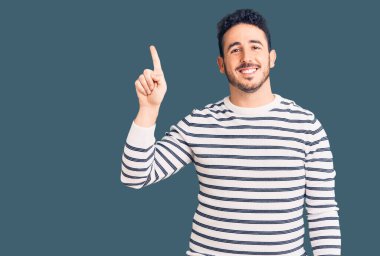 Gündelik kıyafetler giyen genç İspanyol adam başarılı bir fikirle işaret ediyor. Heyecanlı ve mutlu. Bir numara.. 