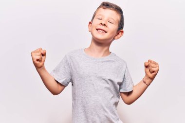 Hoş sarışın çocuk gündelik kıyafetler giyip çok mutlu ve heyecanlı. Kazanan jestler yapıyor. Kolları havada, gülümsüyor ve başarı için bağırıyor. kutlama konsepti. 