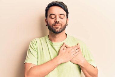 Gündelik kıyafetler giyen genç İspanyol adam elleri göğsünde gülümsüyor, gözleri kapalı ve yüzünde minnet ifadesi var. sağlık kavramı. 