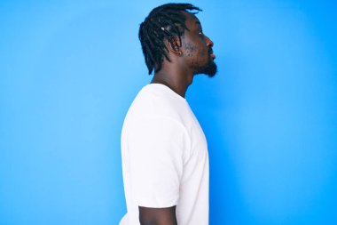 Saçları örgülü, beyaz tişörtlü, rahat bir görünüm takınan, kendine güveni olan genç Afro-Amerikan bir adam.. 