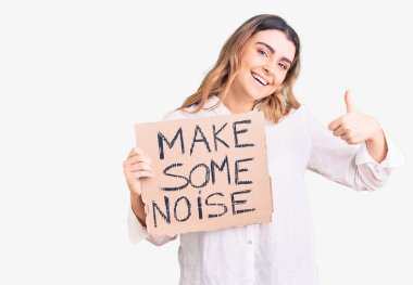 Young caucasian woman holding make some noise banner smiling happy and positive, thumb up doing excellent and approval sign  clipart