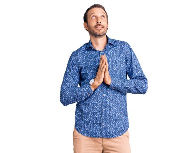 Gündelik giysiler giymiş genç yakışıklı bir adam elleri bağlı yalvarıyor ve dua ediyor. Yüzünde umut ifadesi var. Duygusal ve endişeli. Yalvarıyor. 