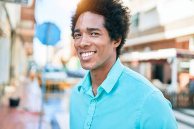 Genç, yakışıklı, Afro-Amerikan bir adam günlük giysiler giyip mutlu gülümsüyor. Yüzünde gülümsemeyle kasaba caddesinde yürürken.