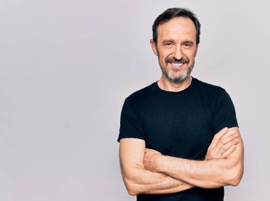 Sıradan siyah tişört giyen orta yaşlı bir adam izole edilmiş beyaz arka planda durup kollarını kavuşturup kameraya bakarken gülümsüyor. Pozitif kişi.