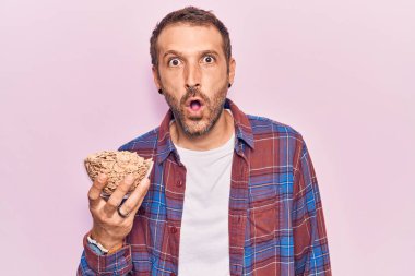 Genç yakışıklı adam mısır gevreği tutuyor. Korkmuş ve ağzı açık kalmış, şaşırmış ve şaşırmış. 