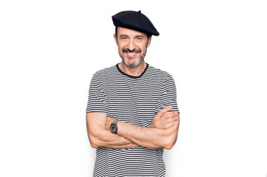 Orta yaşlı, çizgili tişört giyen ve beyaz arka planda Fransız beresi takan, kollarını kavuşturup kameraya bakan yakışıklı bir adam. Pozitif kişi.