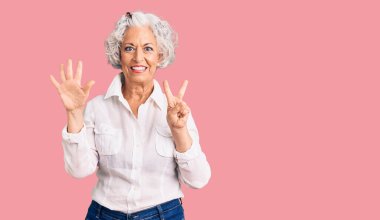 Yaşlı, gri saçlı, günlük kıyafetler giyen, 7 numaralı parmaklarıyla işaret eden, kendinden emin ve mutlu bir kadın.. 
