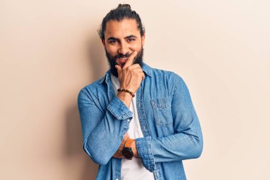 Gündelik giysiler giyen genç Arap adam kameraya kollarını kavuşturup çenesine dokunarak gülümsüyor. Olumlu düşünmek. 