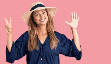 Orta yaşlı İspanyol kadın yaz şapkası takıyor ve yedinci parmaklarını gösterip işaret ederken kendinden emin ve mutlu bir şekilde gülümsüyor.. 