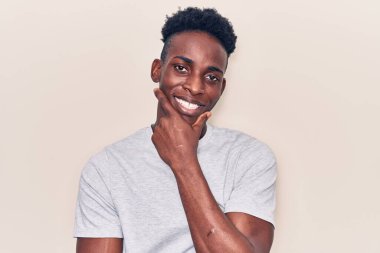 Sıradan kıyafetler giyen genç Afro-Amerikalı adam kameraya kendinden emin bakıyor kollarını kavuşturmuş ve çenesini kaldırmış gülümsüyor. Olumlu düşünmek. 