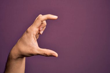 İzole edilmiş mor arka plan üzerinde parmaklarını gösteren beyaz bir adamın eli. Görünmez bir şeyi alıyor, parmakları boşluğu gösteren bir nesneyi tutuyor.