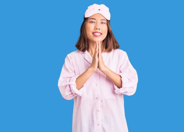 Genç güzel Çinli kız uyku maskesi takmış ve pijama giymiş ellerle dua ederek af diliyor kendinden emin bir şekilde gülümsüyor.. 