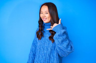 Kış süveteri giyen genç, güzel bir Çinli kız telefonla el ve parmak hareketleriyle gülümsüyor, telefonda konuşuyor gibi. iletişim kavramları. 