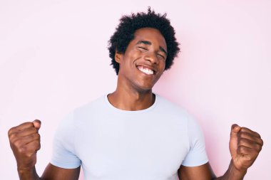 Yakışıklı Afro saçlı, sıradan kıyafetler giyen, çok mutlu ve heyecanlı kolları havada, gülümseyen ve başarı için bağıran afrikalı bir Amerikalı. kutlama konsepti. 