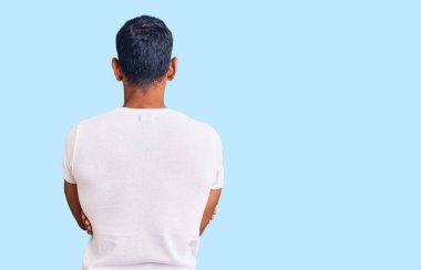 Gündelik kıyafetler giyen genç latin adam kollarını kavuşturup arkaya bakıyor. 