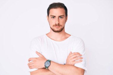 Sıradan beyaz tişört giyen, kuşkucu ve gergin genç yakışıklı bir adam. Yüzünde çapraz kollu tasvip etmeyen bir ifade var. negatif kişi. 