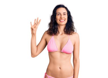 Genç ve güzel İspanyol kadın bikini giyip parmaklarıyla dört numarayı gösterirken kendinden emin ve mutlu bir şekilde gülümsüyor.. 