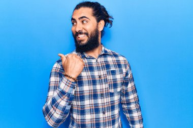 Gündelik kıyafetler giyen, gülen yüzlü genç bir Arap başparmağıyla yan tarafa bakıyor ve işaret ediyor.. 