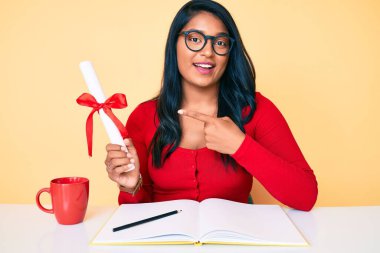 Uzun saçlı, diplomalı, güzel Latin bir kadın. Gülümsüyor, mutlu bir el ve parmak ile işaret ediyor. 