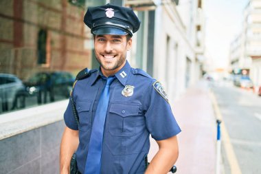 Polis üniforması giyen genç, yakışıklı İspanyol polis mutlu bir şekilde gülümsüyor..
