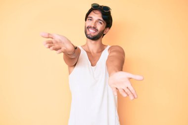 Yaz bakışı ve güneş gözlüğü takan yakışıklı İspanyol adam sarılmak için kollarını açmış gülümseyen kameraya bakıyor. Mutluluğu kucaklayan neşeli bir ifade.. 