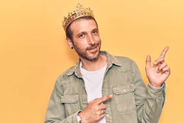 Kral tacını takan yakışıklı genç adam gülümsüyor ve kameraya bakıyor iki eliyle ve parmaklarıyla kenarı işaret ediyor.. 