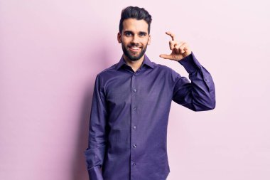 Sakallı, rahat gömlekli, gülümseyen, kendine güvenen, el hareketi yapan, parmaklarıyla işaret eden ve kameraya bakan genç yakışıklı bir adam. ölçüm kavramı. 