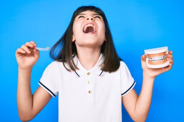 Gürültülü küçük kız görünmez hizayı tutuyor ve diş telleri kızgın ve öfkeli çığlıklar atıyor öfkeyle bağırıyor, öfkeyle yukarı bakıyor. 