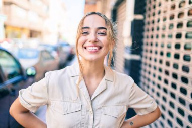 Genç, güzel, sarışın, beyaz bir kadın güneşli bir günde mutlu bir şekilde gülümsüyor.