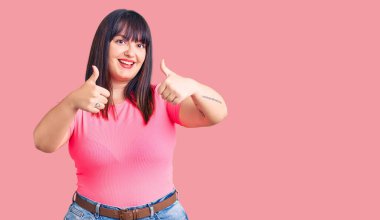 Genç ve cüsseli bir kadın gündelik giysiler giyip olumlu jestler yapıyor. Elleriyle gülümsüyor ve başarı için seviniyor. kazanan jest. 