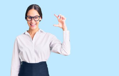 Güzel, esmer, profesyonel garson önlüğü giyen, gülümseyen, kendine güvenen, el hareketi yapan, parmaklarıyla işaret yapan ve kameraya bakan bir kadın. ölçüm kavramı. 