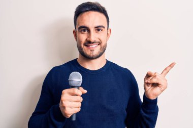 Sakallı genç yakışıklı şarkıcı beyaz arka planda mikrofon kullanarak şarkı söylüyor.