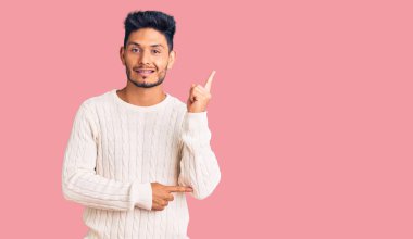 Yakışıklı Latin Amerikalı sıradan bir kazak giyen genç adam gülümsüyor mutlu bir şekilde elini ve parmağını yana uzatıyordu. 