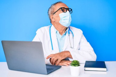 Gri saçlı, doktor üniforması giyen ve sağlık maskesi takmış yüzünde gülümseme, doğal bir ifade olan son sınıf yakışıklı bir adam. Kendinden emin gülen. 