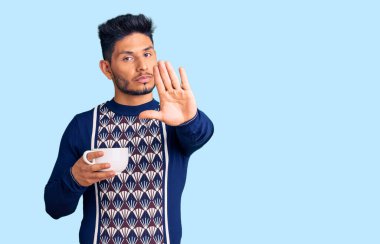 Yakışıklı Latin Amerikalı genç adam. Açık elle bir fincan kahve içiyor. Dur işareti yapıyor. 