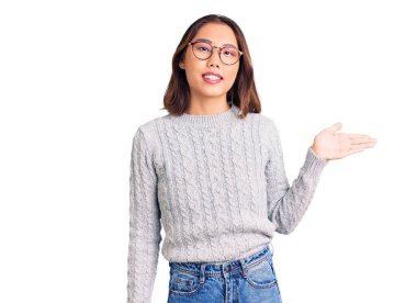 Genç, güzel Çinli bir kız günlük kıyafetler giymiş neşeli bir şekilde gülümsüyor ve avuç içi kameraya bakıyor.. 