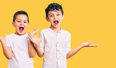 İki küçük kardeş birlikte günlük kıyafetler giyip zaferi kutluyorlar mutlu bir gülümsemeyle ve ellerini kaldırarak kazanan bir ifadeyle. 