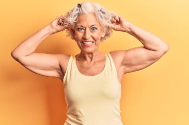 Kıdemli gri saçlı kadın, günlük kıyafetler giyiyor, gülümsüyor kulakları parmaklarıyla çekiyor, komik bir jest. deneme sorunu 