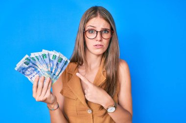 Güney Afrika rand banknotlarını elinde tutan genç sarışın kız hiçbir şey bilmiyor ve kafası karışık. şüphe kavramı. 