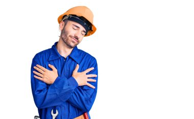 Genç İspanyol işçi üniforması giyen mutlu ve olumlu bir şekilde kendine sarılan, kendinden emin gülümseyen. Sevgi ve özgüven. 