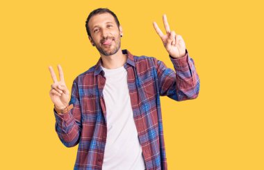 Gündelik kıyafetler giyen, dili açık gülümseyen ve zafer işareti yapan genç yakışıklı bir adam. İki numara.. 